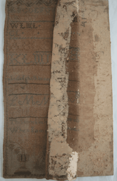 Embroidered sampler shown partially covered by a degraded, peeling backing layer revealing the original stitched surface beneath.